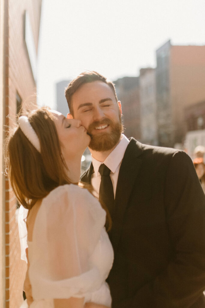 A bride kissing her grooms cheek while eloping in the city who used wedding planning tips