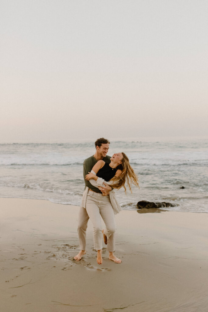 An engaged couple laughing on the beach during their engagement photo session after learning wedding planning tips 