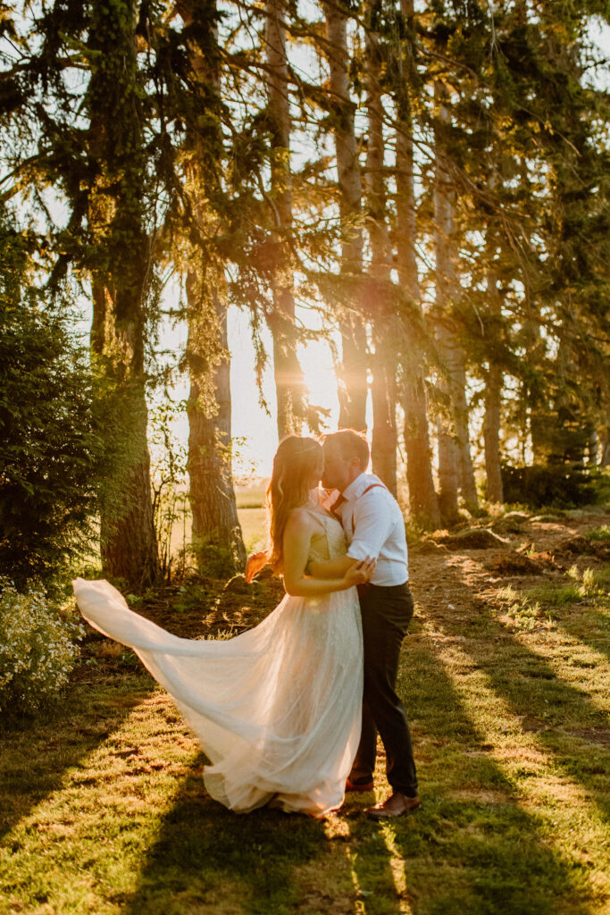 A bride and groom at sunset kissing with her dress flying in the air after learning wedding planning tips 
