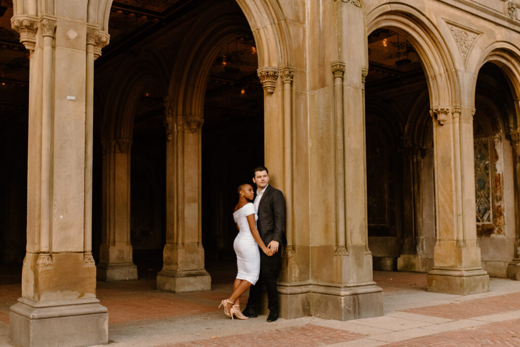An engaged couple standing under an archway in New York City celebrating their engagement after learning wedding planning tips 