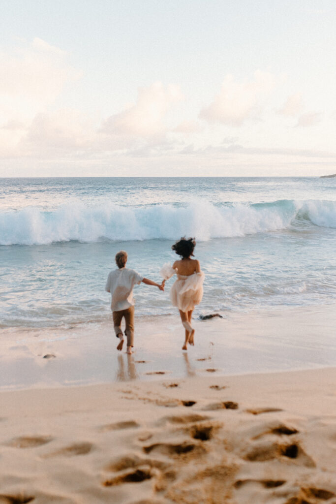 An engaged couple running into the ocean during their engagement session in Hawaii after learning wedding planning tips 