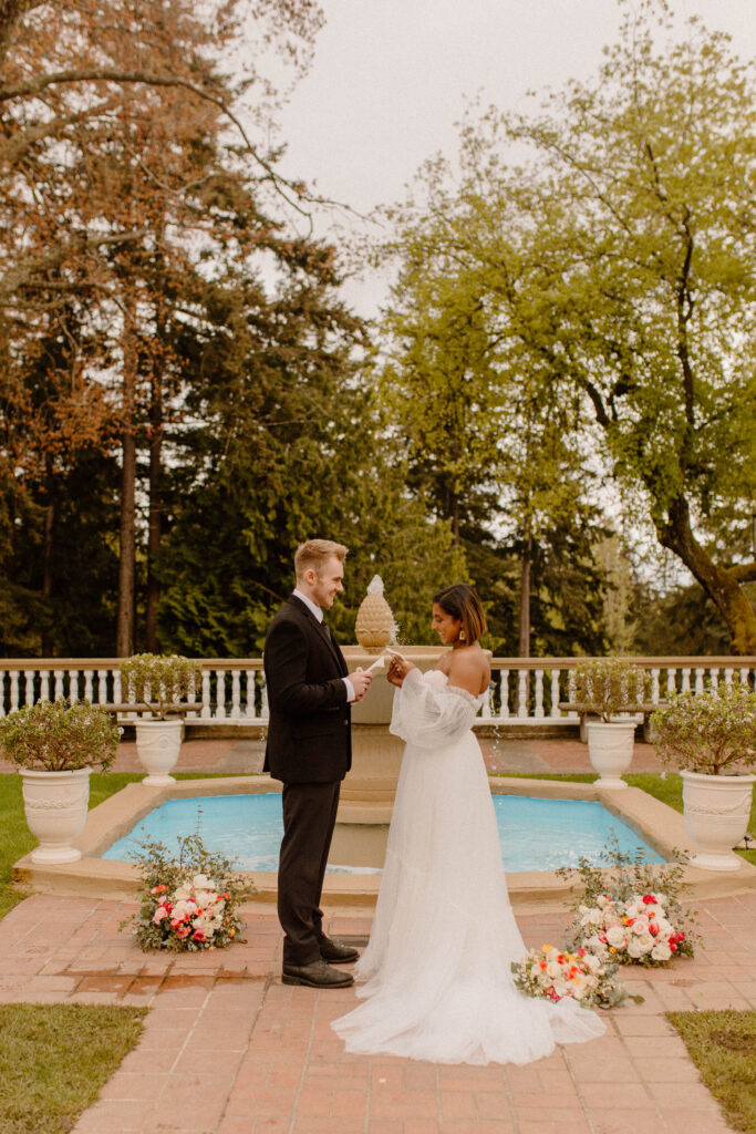 A bride and groom reading their vows to each other in front of a fountain at their Washington garden venue after learning wedding planning tips 