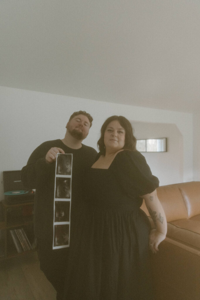 Couple leaning against their couch during their in home pregnancy announcement photoshoot.