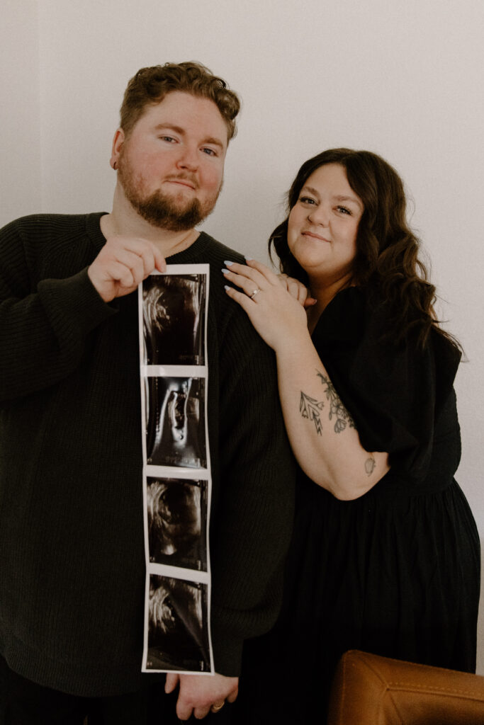 Couple snuggling up holding their ultrasound picture for their in home pregnancy announcement photoshoot.