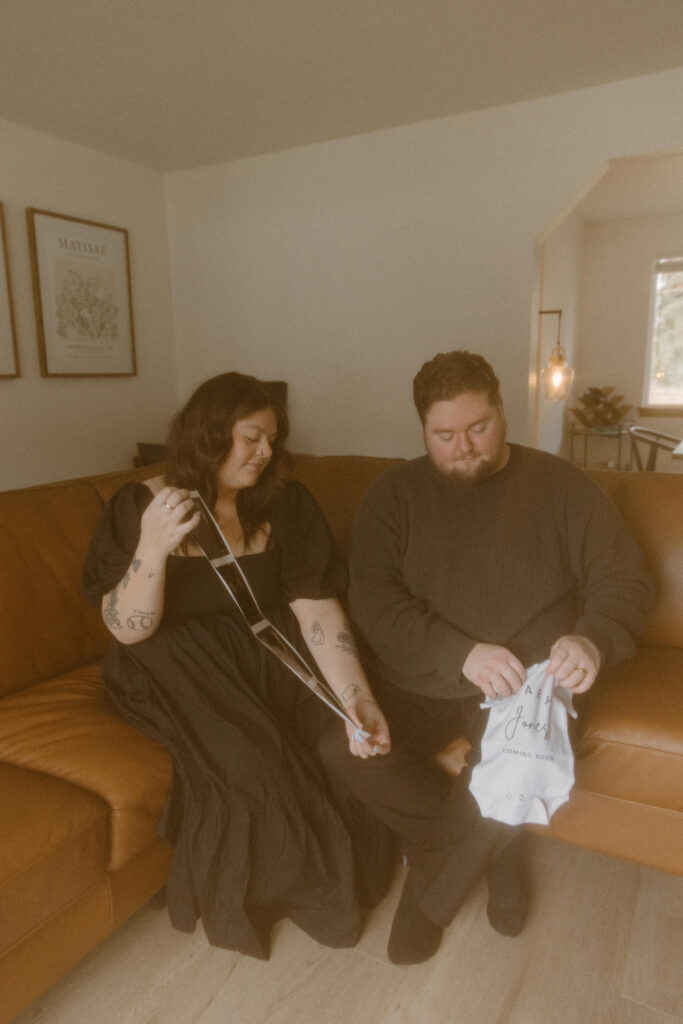 Married couple announcing their pregnancy in home on their couch.