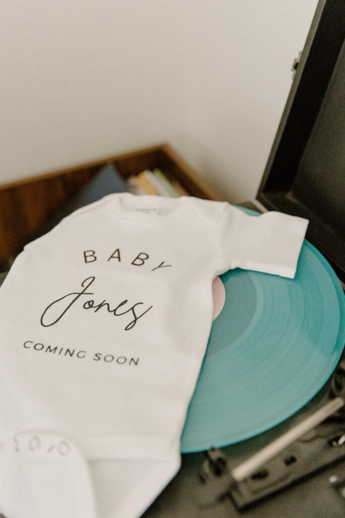 A blue record and a baby onsie photographed to announce pregnancy. 