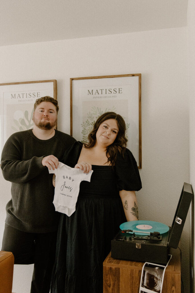 Record player pregnancy announcement of a couple holding a onsie.