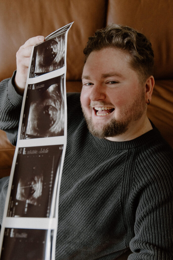 A man holding an ultrasound smiling to announce him and his partner is having a baby.
