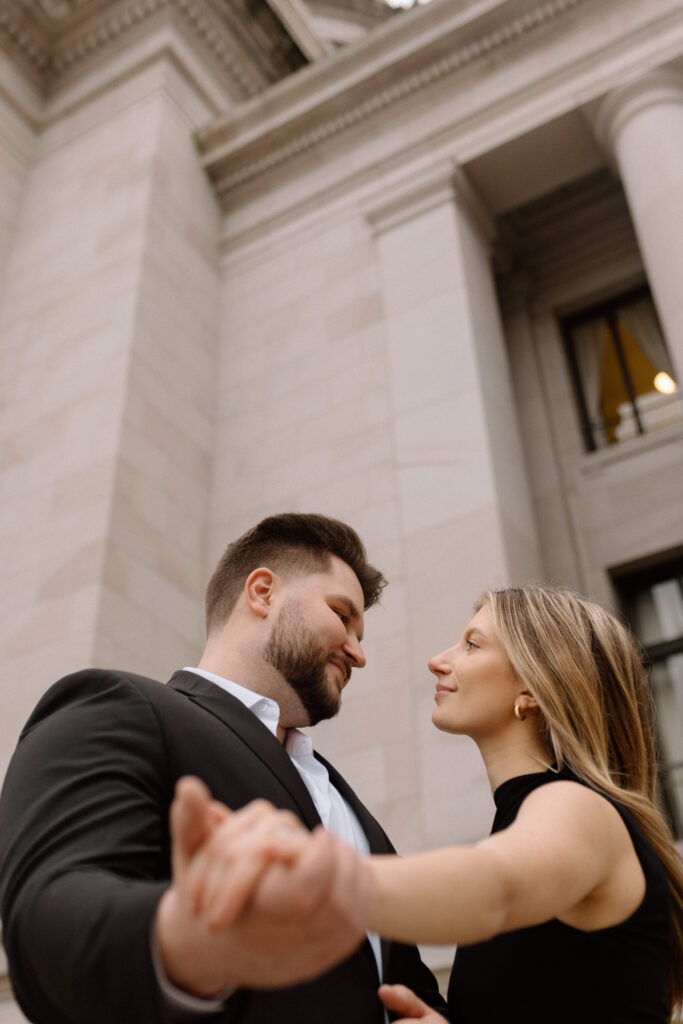 A couple holding hands facing each other posing for their classic engagement photos.