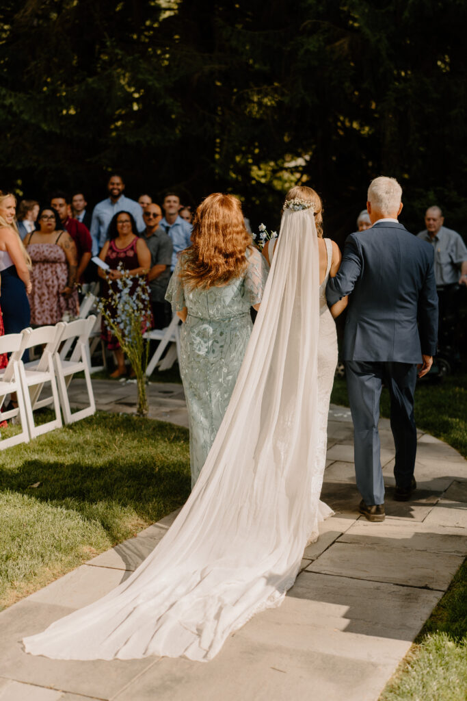 bride walking down the aisle with parents at her intimate summer wedding