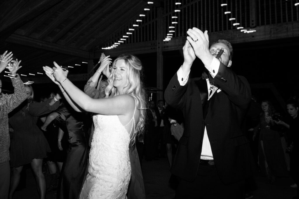 black and white wedding photo of bride and groom dancing and clapping while smiling on the dance floor