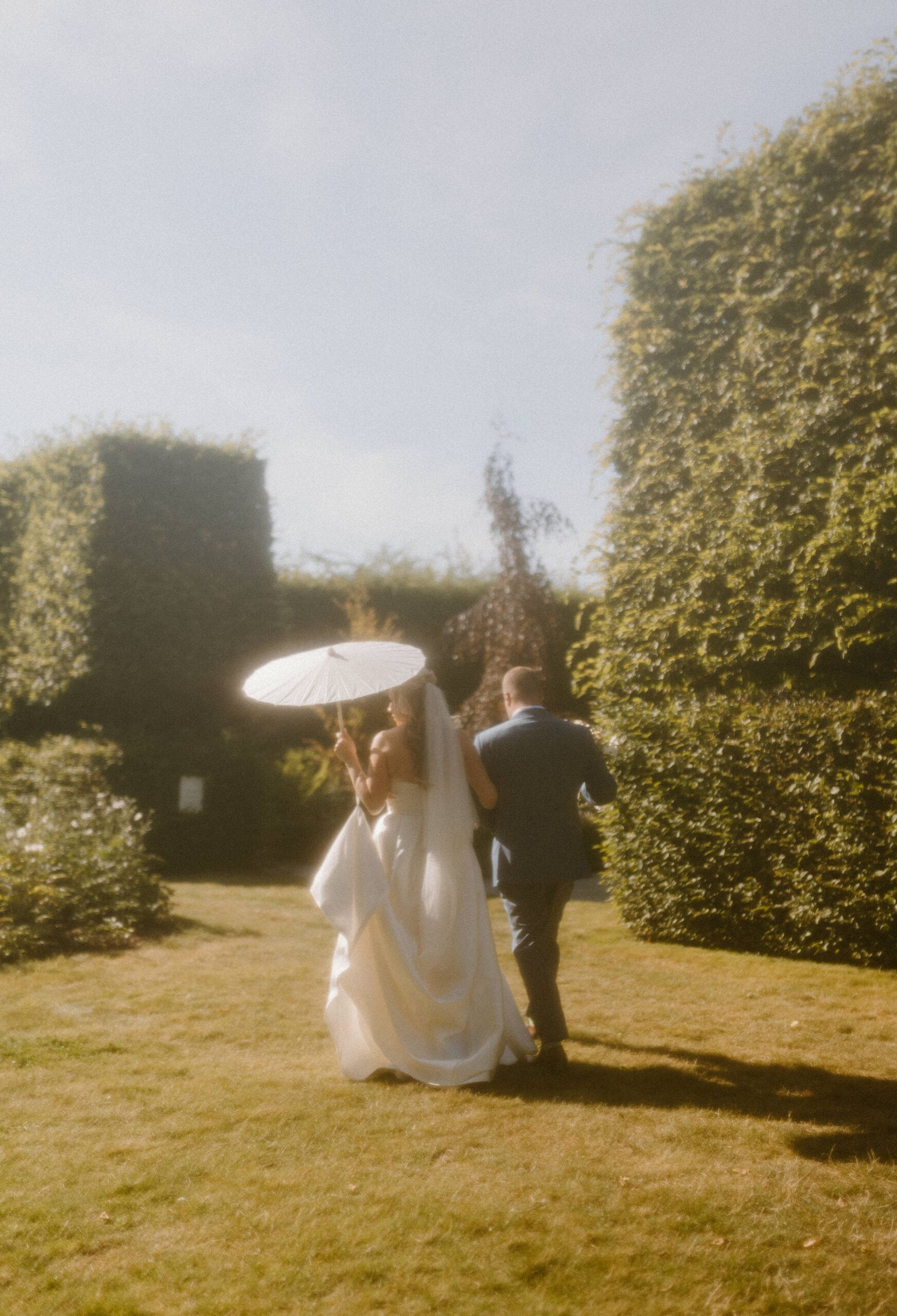 Bride and groom on a sunny summer day walking through the garden grounds in their wedding attire.